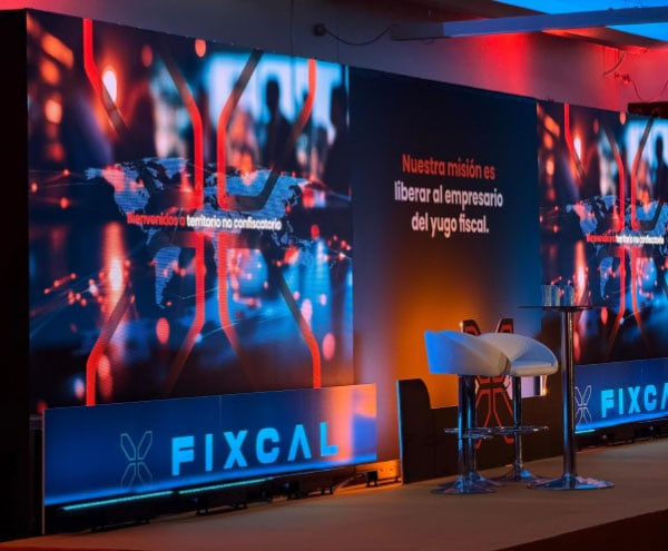 Escenario de evento con pantallas y mobiliario en FICXAL, tecnología y networking.
